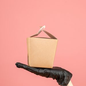 top-view-wearing-black-glove-hand-holding-small-box-pastel-peach